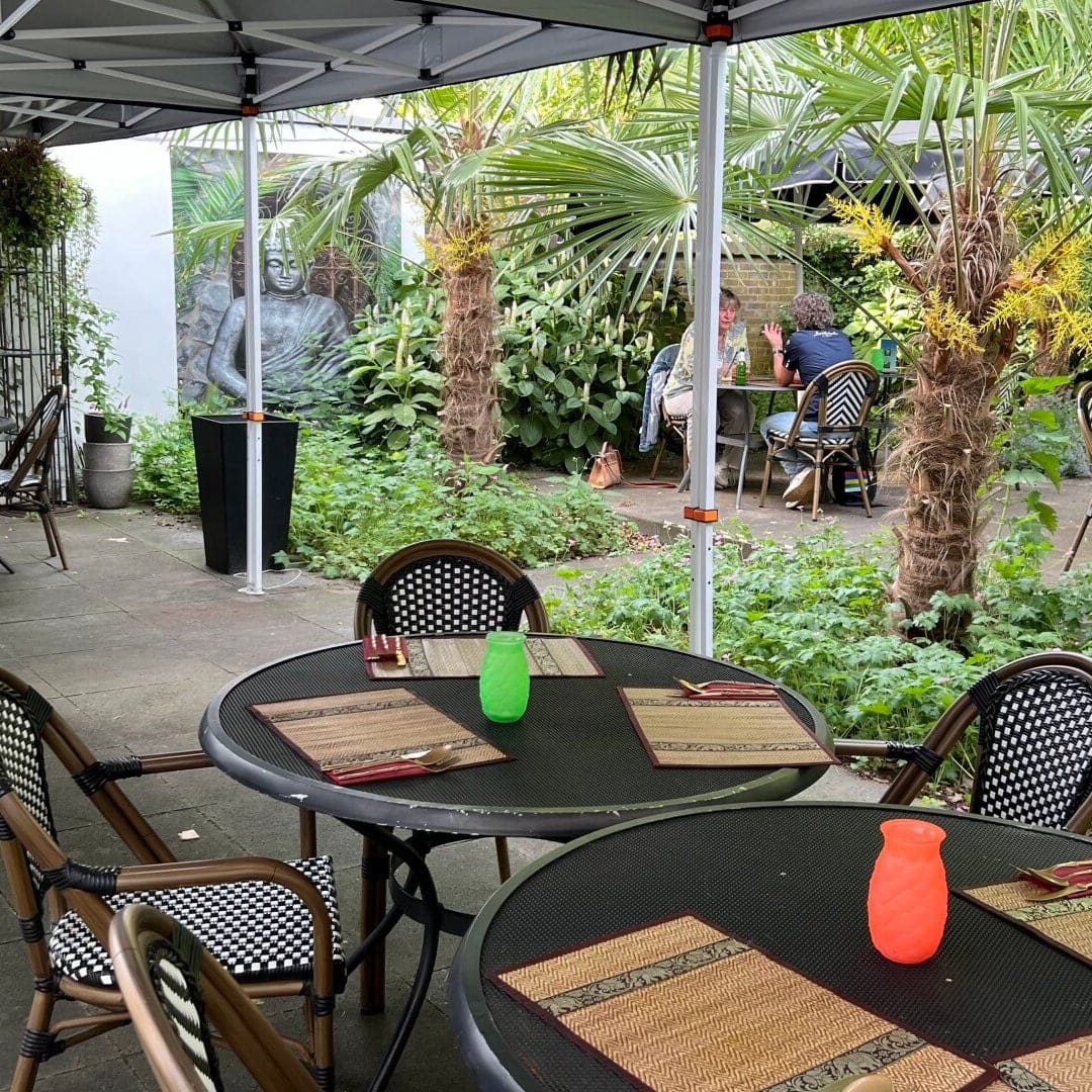 Ronde terrastafels onder een partytent tussen de palmen in de binnentuin.