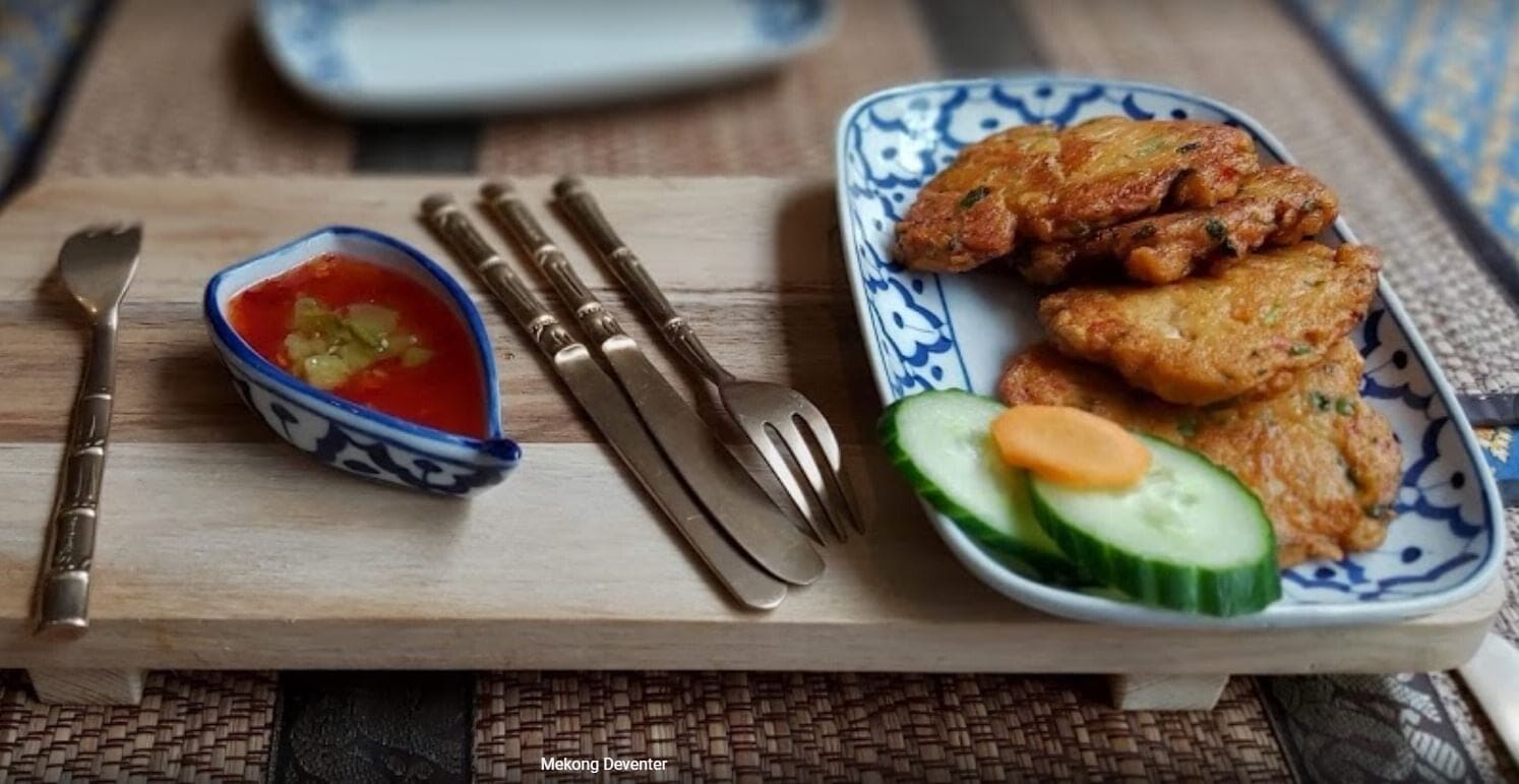 Thaise viskoekjes met komkommer en zoetzure saus op een houten plankje.