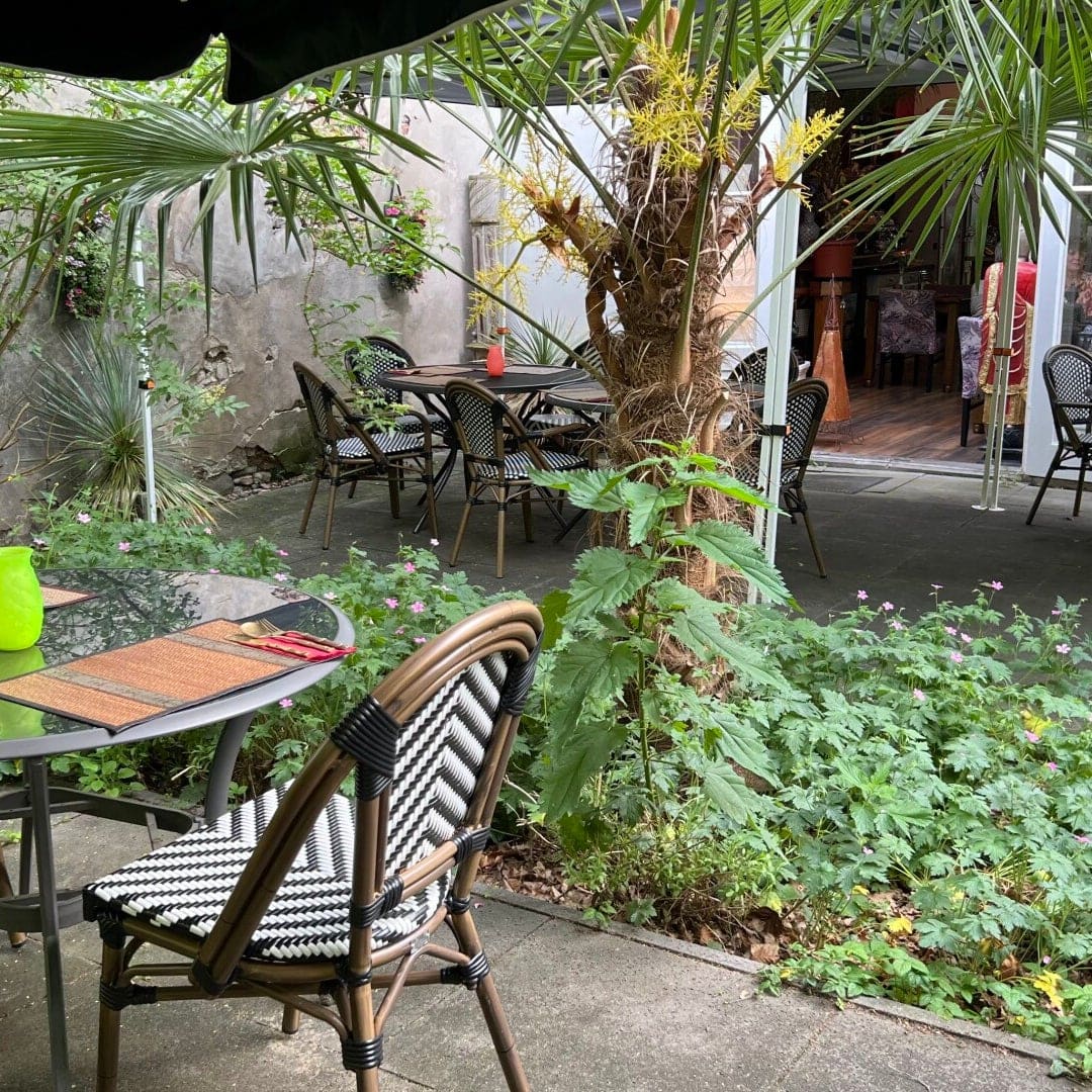 Het terras in de binnentuin, met palmen, een oude stadsmuur en gedekte tafels.