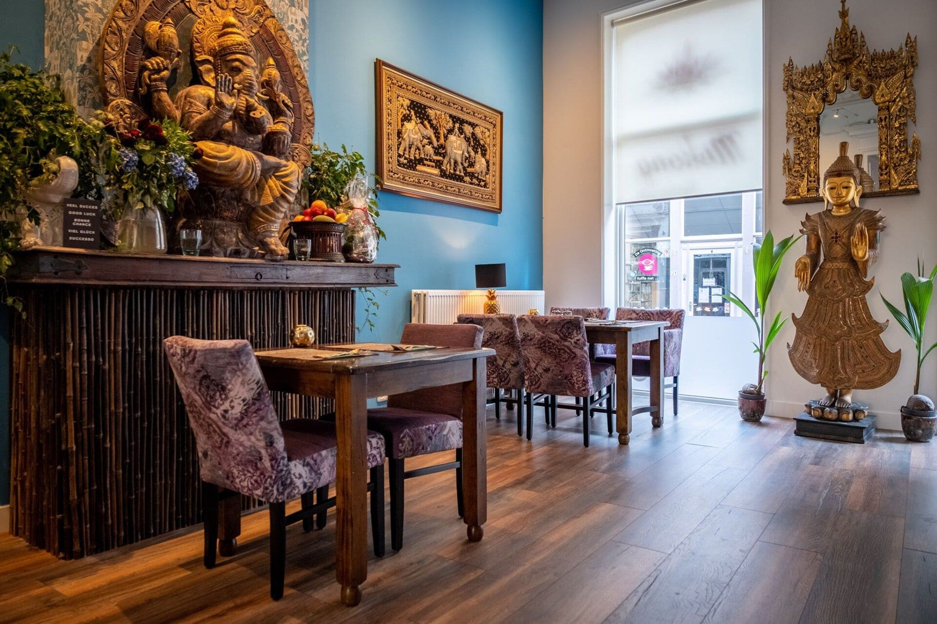 De blauwe eetzaal met een gouden Ganeshabeeld, bamboe wandpaneel en paarse stoelen.