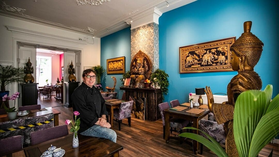 De blauwe eetzaal van Mekong Deventer met gouden beelden, orchideeën en gedekte tafels.