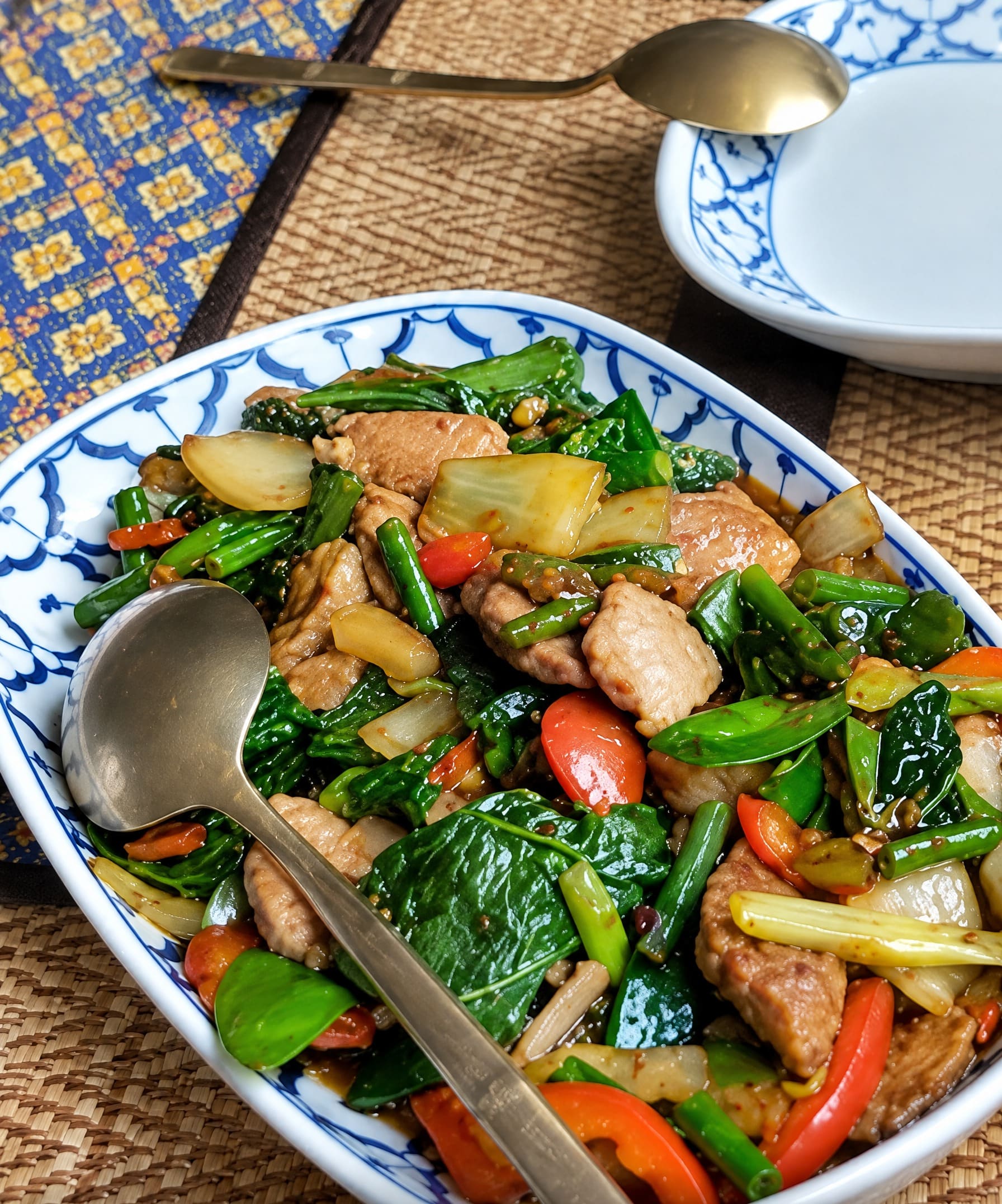 Thais wokgerecht met vlees, verse groente en pepers op een blauw met wit bord.