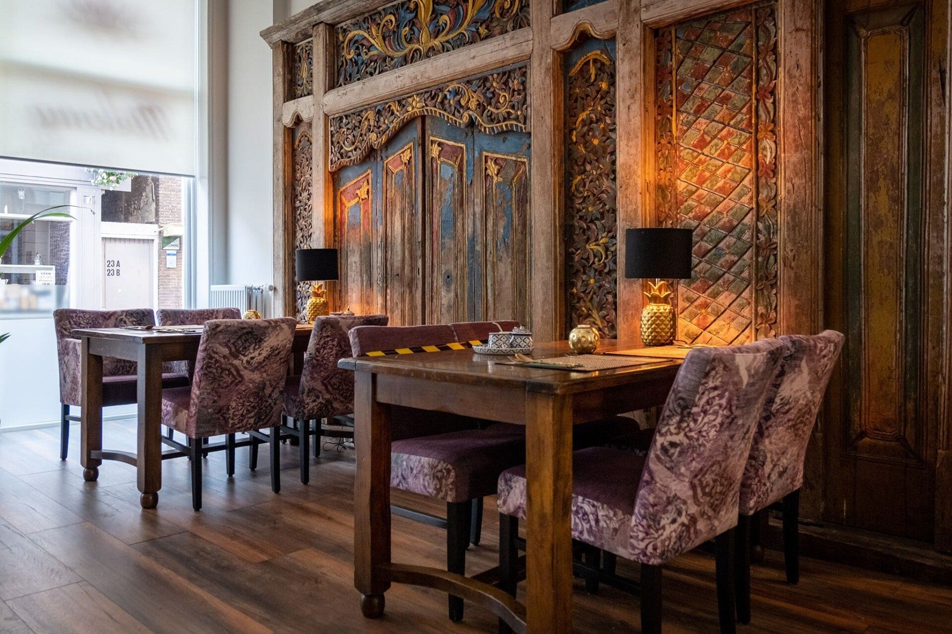Oude houtsnijwerk panelen in blauw, rood en goud als wand achter de gedekte tafels.